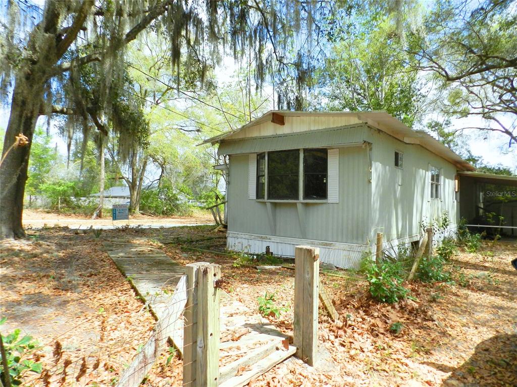 A weathered, light-green mobile home sits on a wooded lot with a wooden walkway — 755 SW JASMINE AVENUE, KEYSTONE HEIGHTS, FL
