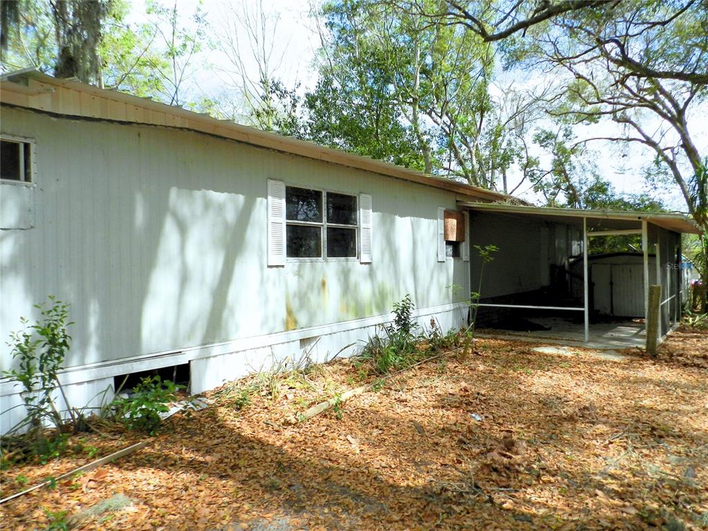 The exterior of a weathered mobile home features metal siding, a screened porch, and leaf-covered ground — 755 SW JASMINE AVENUE, KEYSTONE HEIGHTS, FL