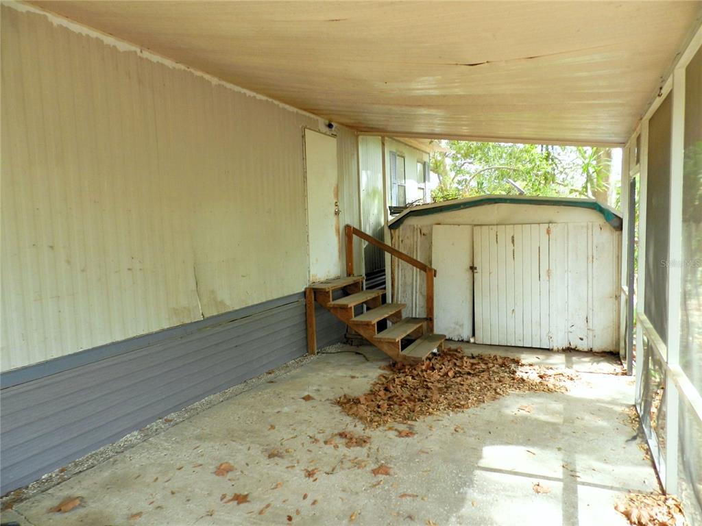 A covered concrete carport features wooden stairs leading to a door and a storage shed — 755 SW JASMINE AVENUE, KEYSTONE HEIGHTS, FL