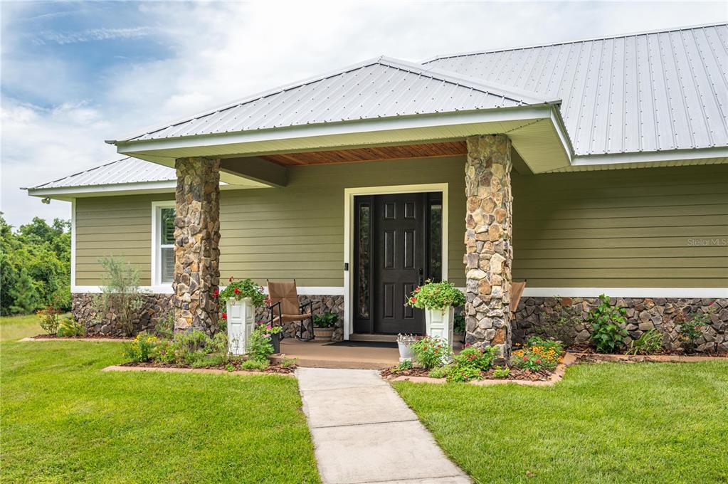 A house exterior with olive green siding, stone accents, a metal roof, and a front porch — 3629 GREAT MASTERPIECE ROAD, LAKE WALES, FL