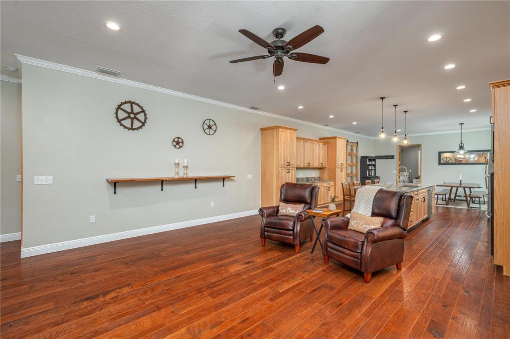 An open-concept living area features wood floors, two leather armchairs, and a kitchen with wooden cabinets — 3629 GREAT MASTERPIECE ROAD, LAKE WALES, FL