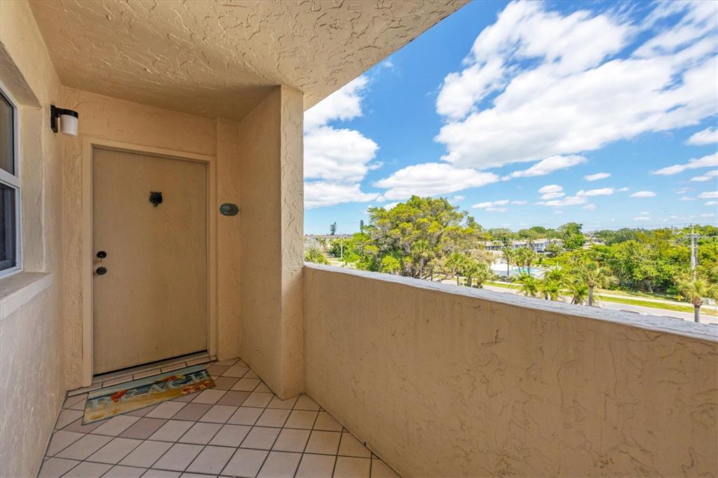 An outdoor balcony features a beige door, tiled flooring, and a view of trees — 4325 GULF OF MEXICO DRIVE UNIT 408, LONGBOAT KEY, FL