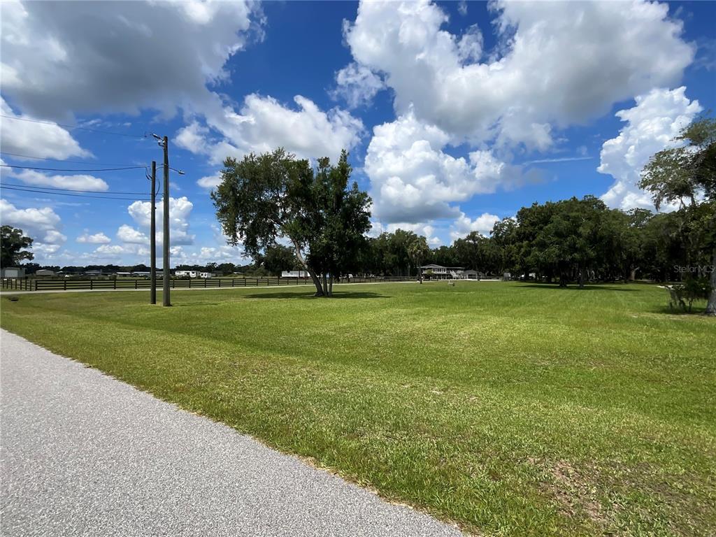 A grassy, open field features scattered trees, a wooden fence, and utility poles — 3180 CANTER LANE, KISSIMMEE, FL