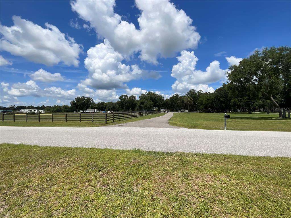 A paved driveway leads through a grassy field toward a fenced property with mature trees — 3180 CANTER LANE, KISSIMMEE, FL