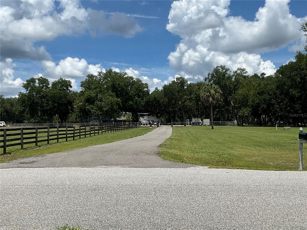 A paved driveway leads toward a house behind a wooden fence on a grassy lot — 3180 CANTER LANE, KISSIMMEE, FL