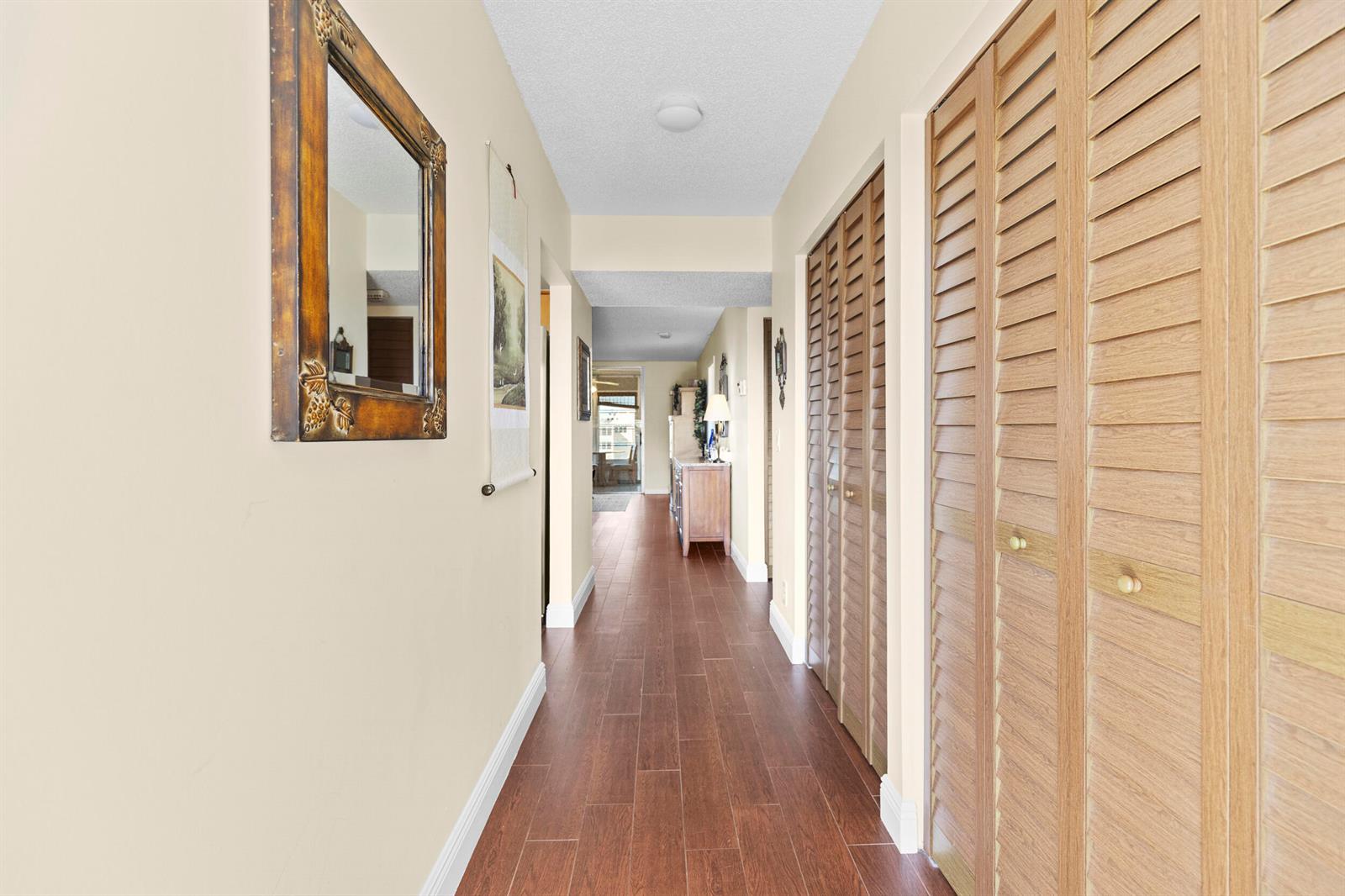 A hallway features wood-look tile flooring, beige walls, and louvered closet doors on the right — 14671 Bonaire Boulevard # 404, Delray Beach FL 33446, DELRAY BEACH, FL