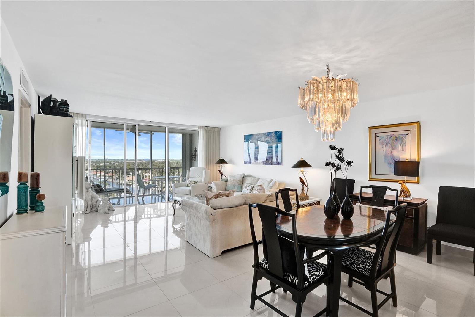 A bright living and dining area with white tile floors, a crystal chandelier, and balcony — 303 N Riverside Drive, Pompano Beach FL 33062, POMPANO BEACH, FL