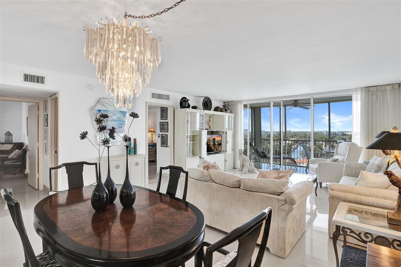 A dining and living area features a crystal chandelier, dark wood table, and balcony view — 303 N Riverside Drive, Pompano Beach FL 33062, POMPANO BEACH, FL