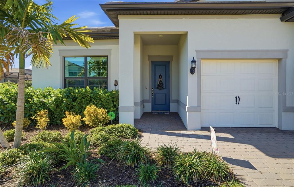 The exterior of a single-story home features a blue front door and a white garage — 16408 PEBBLE RIDGE DRIVE, BRADENTON, FL
