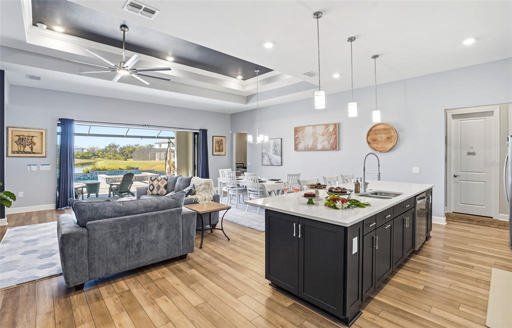 A modern open-concept living area features a kitchen island, dining space, and sliding glass doors — 16408 PEBBLE RIDGE DRIVE, BRADENTON, FL