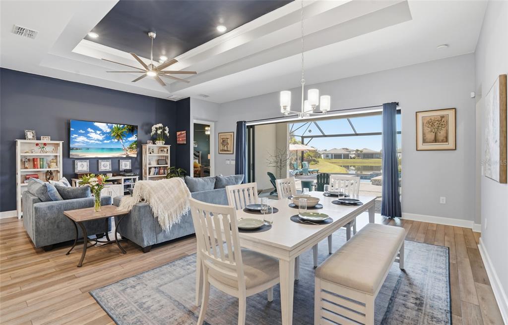 An open-concept living and dining area features a tray ceiling, dark accent wall, and pool view — 16408 PEBBLE RIDGE DRIVE, BRADENTON, FL
