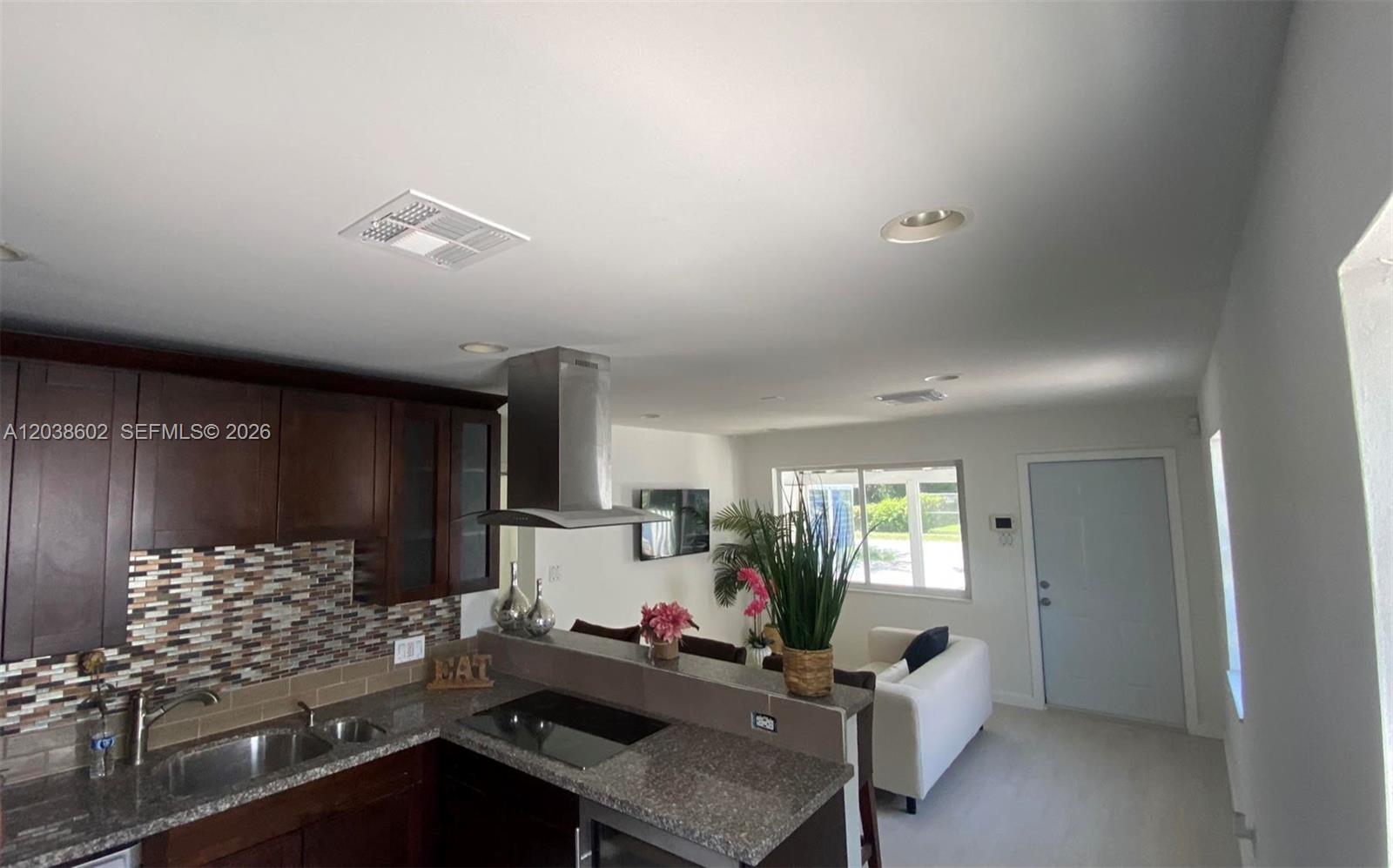 A kitchen with dark wood cabinets and granite countertops overlooks a living area — 1947 Garfield St, Hollywood FL 33020, HOLLYWOOD, FL