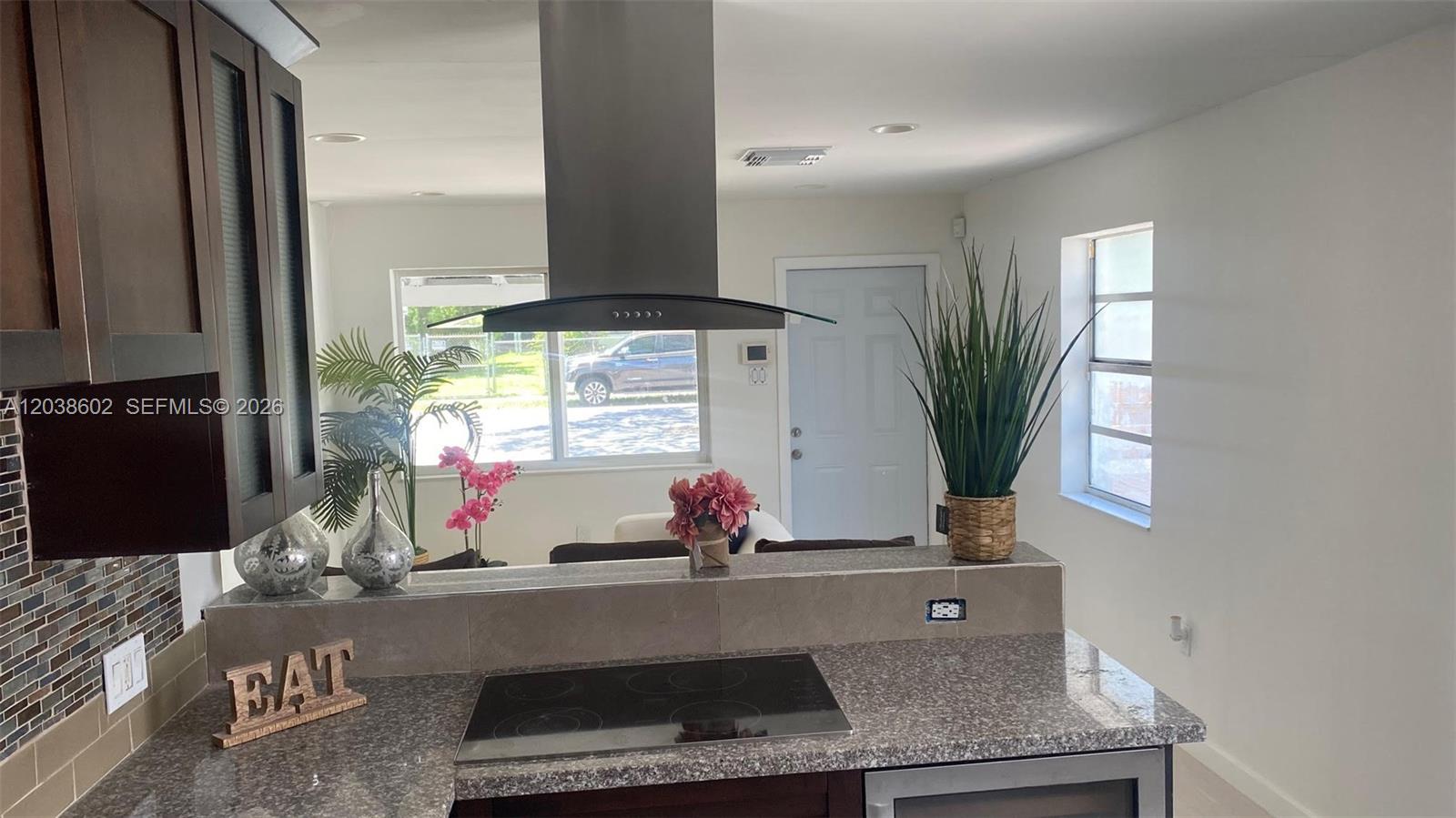 A kitchen features granite countertops, a glass cooktop, a stainless steel hood, and dark cabinetry — 1947 Garfield St, Hollywood FL 33020, HOLLYWOOD, FL