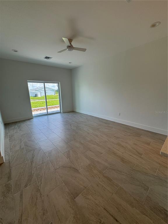 An empty room features light-colored tile flooring, a ceiling fan, and a sliding glass door — 10490 PENDLETON AVENUE, ENGLEWOOD, FL