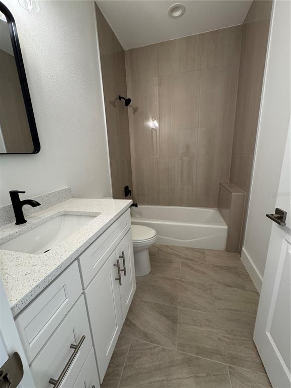 A bathroom features a white vanity with a speckled countertop, a toilet, and a tub-shower — 10490 PENDLETON AVENUE, ENGLEWOOD, FL
