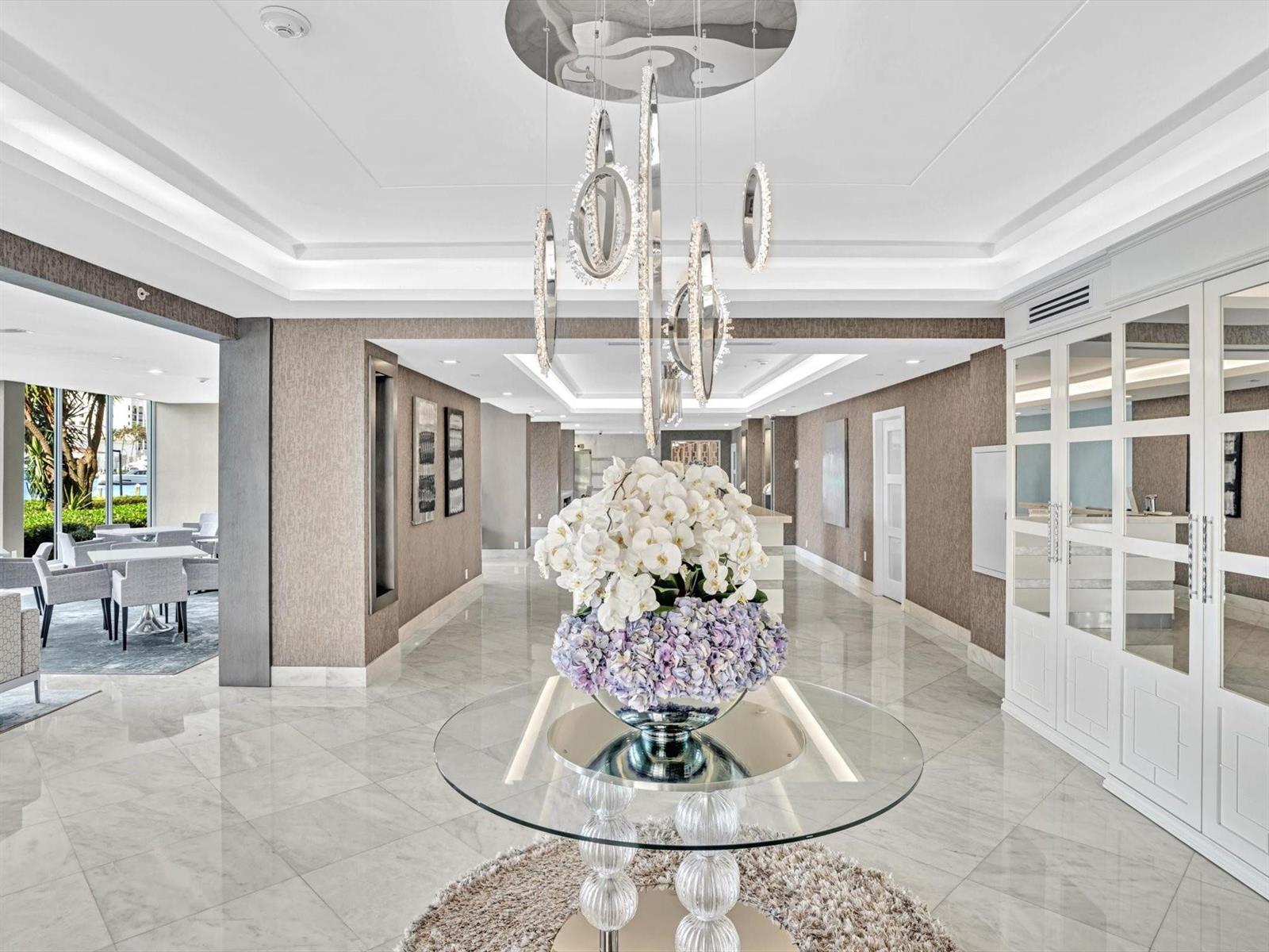 A modern lobby features a glass table with floral arrangements, marble floors, and hanging lights — 701 E Camino Real # 4e, Boca Raton FL 33432, BOCA RATON, FL