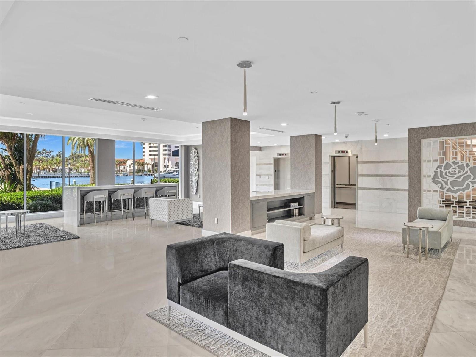 A modern lobby features gray velvet seating, marble floors, and a bar overlooking a waterway — 701 E Camino Real # 4e, Boca Raton FL 33432, BOCA RATON, FL