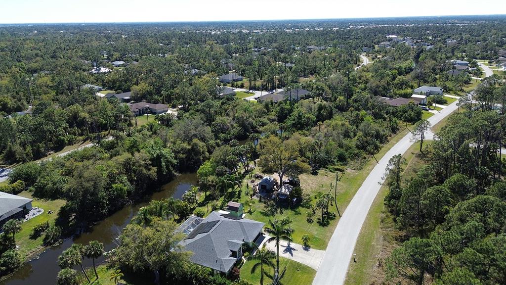 An aerial view shows a house with a pool cage next to a canal and road — NAMATKA AVENUE, NORTH PORT, FL