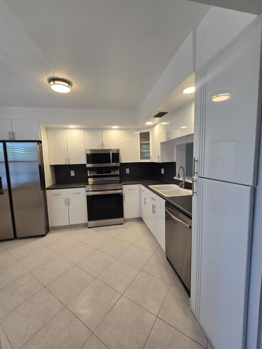 A kitchen features white cabinetry, stainless steel appliances, dark countertops, and light-colored tile flooring — 3301 Aruba Way # K2, Coconut Creek FL 33066, COCONUT CREEK, FL
