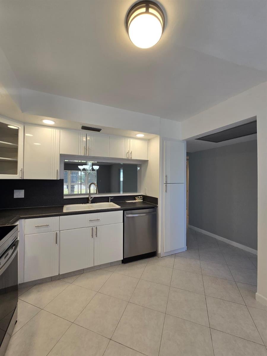 A kitchen features white cabinets, black countertops, stainless steel appliances, and light-colored tile flooring — 3301 Aruba Way # K2, Coconut Creek FL 33066, COCONUT CREEK, FL