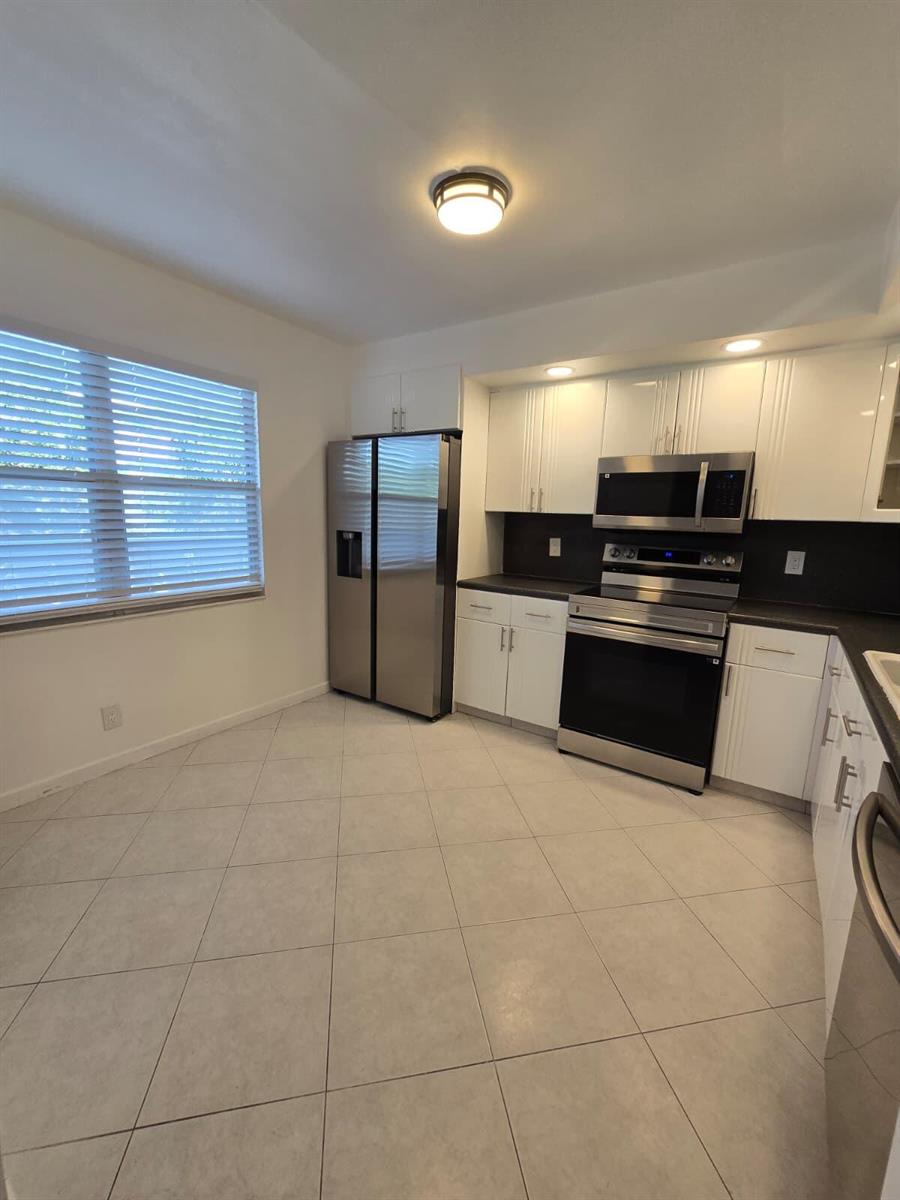 A kitchen features white cabinets, stainless steel appliances, and light-colored tile flooring — 3301 Aruba Way # K2, Coconut Creek FL 33066, COCONUT CREEK, FL