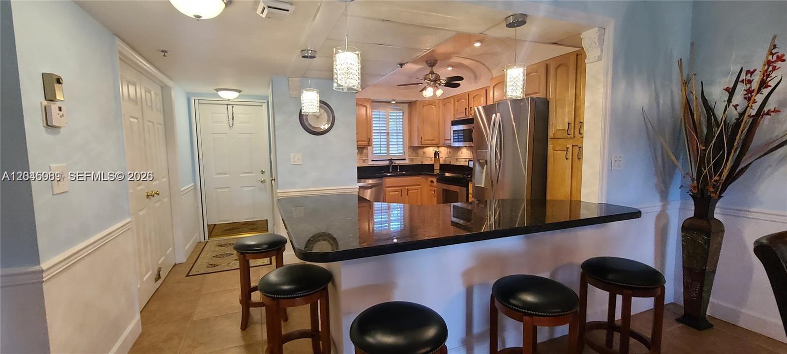 A kitchen with a black granite breakfast bar, wooden cabinets, and stainless steel appliances — 3300 W Rolling Hills Cir # 104, Davie FL 33328, DAVIE, FL