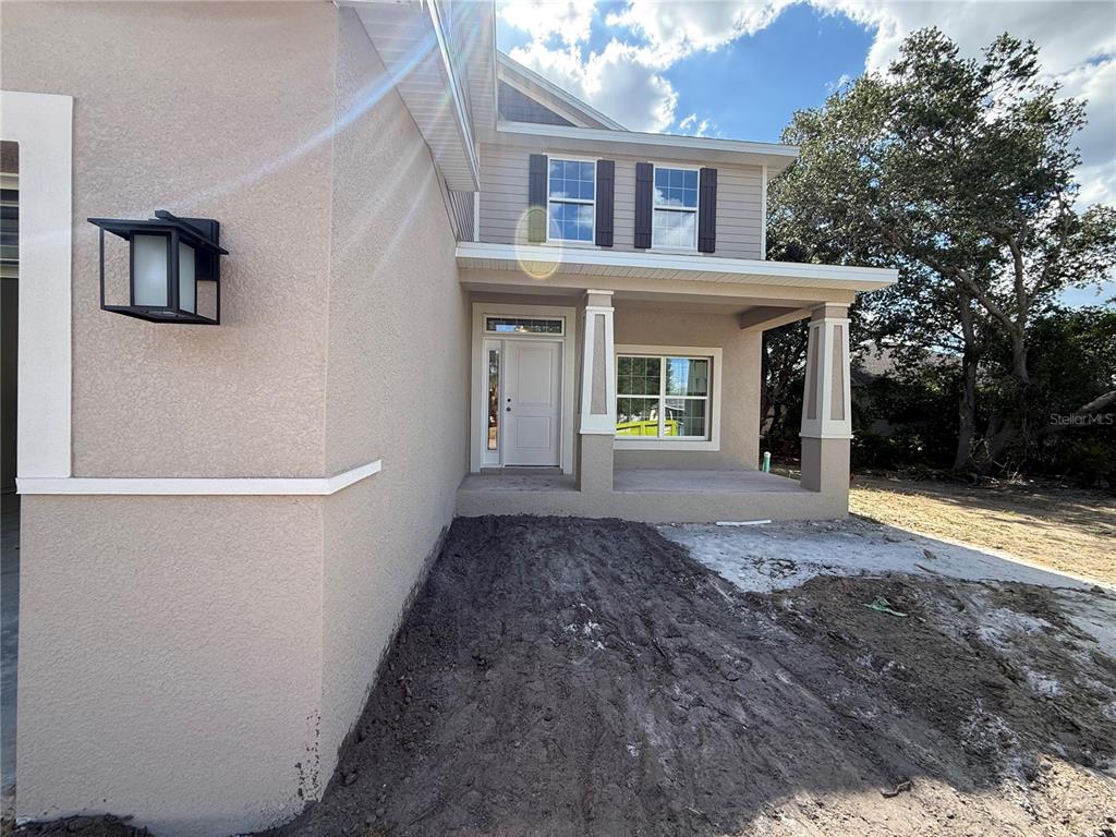 A tan two-story house features a covered front porch, dark shutters, and unfinished dirt landscaping — 453 SAN AMBROSIO STREET, PUNTA GORDA, FL