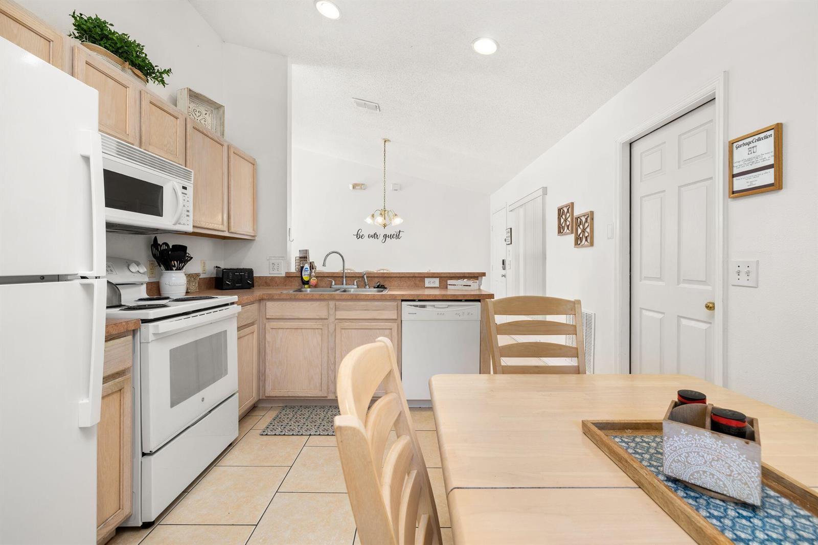 A kitchen features light wood cabinets, white appliances, tile flooring, and an adjacent dining area — 128 Pine Cone Drive, Davenport FL 33897, DAVENPORT, FL