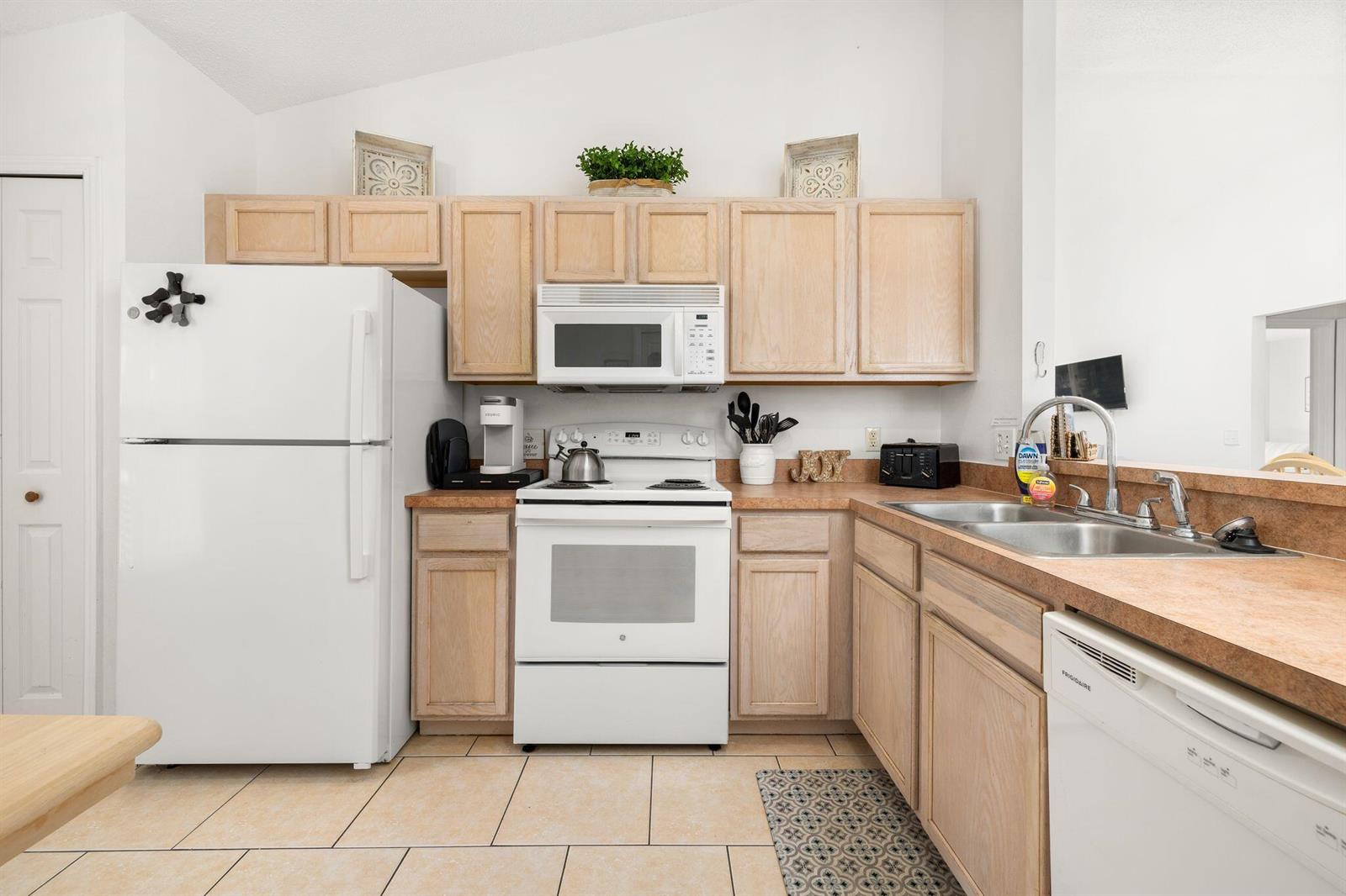 A kitchen with light wood cabinets, white appliances, and tan countertops — 128 Pine Cone Drive, Davenport FL 33897, DAVENPORT, FL
