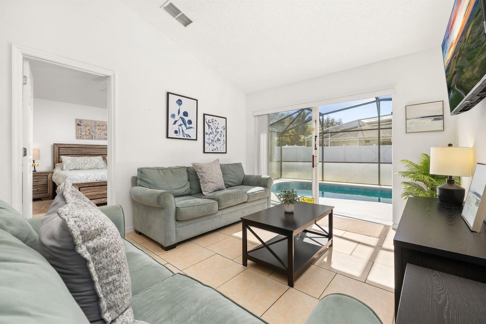 A living room with light tile floors, teal sofas, and a sliding door to a pool — 128 Pine Cone Drive, Davenport FL 33897, DAVENPORT, FL