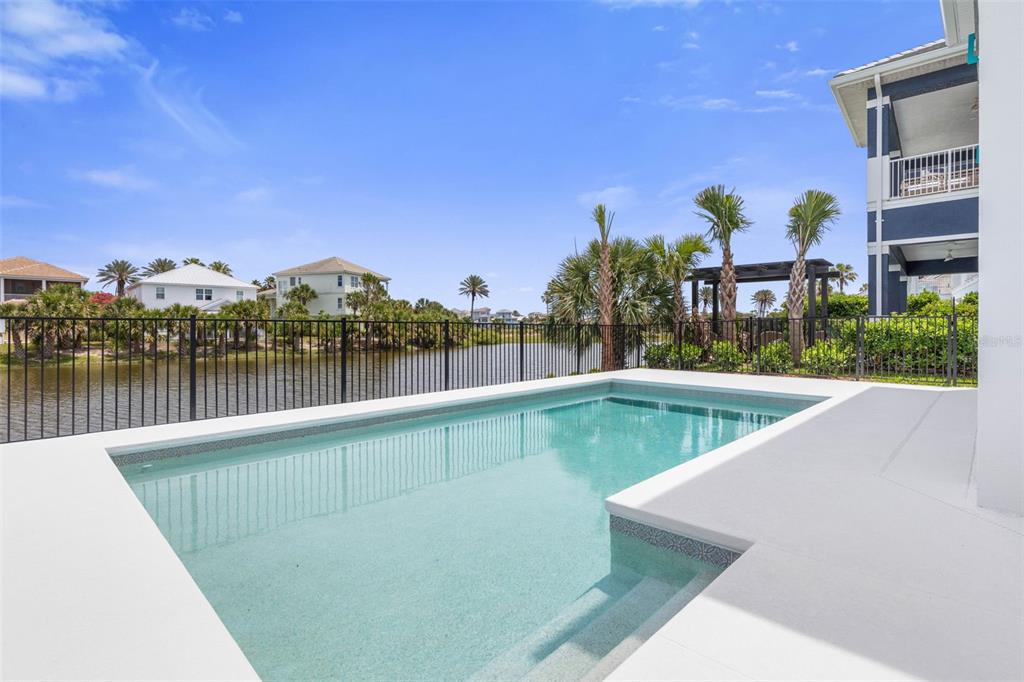 A rectangular swimming pool sits on a white patio overlooking a lake and palm trees — 24 CINNAMON BEACH WAY, PALM COAST, FL
