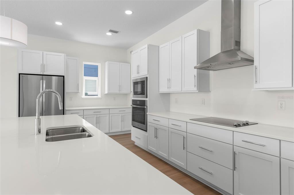 A modern kitchen features white cabinetry, stainless steel appliances, and a large quartz-topped island — 24 CINNAMON BEACH WAY, PALM COAST, FL