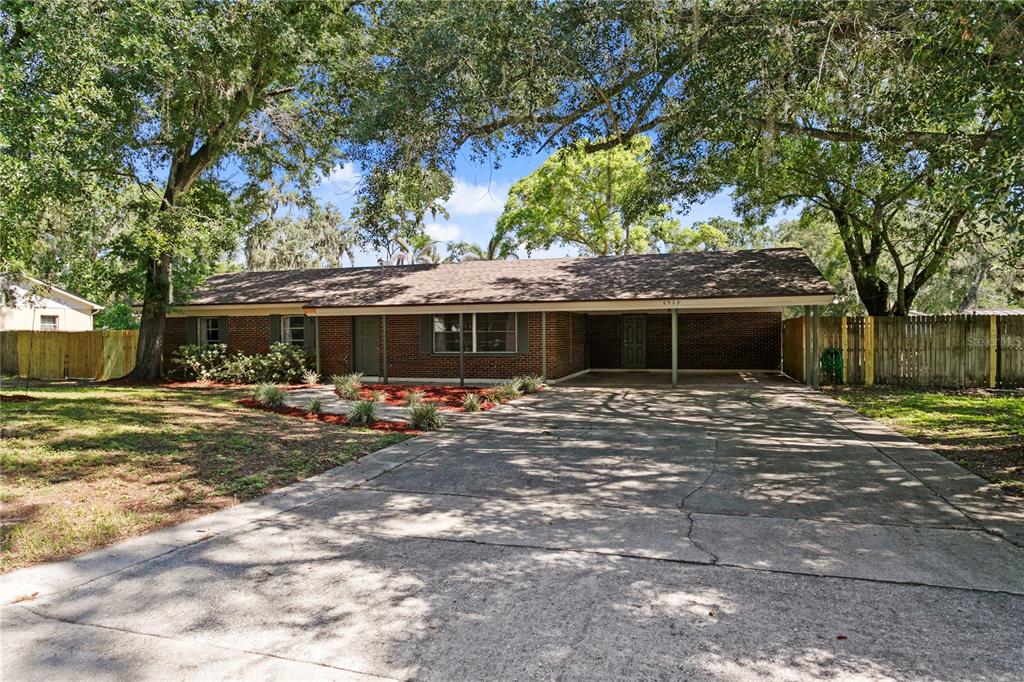 A single-story brick house features a large concrete driveway and an attached carport — 6928 GREENHILL PLACE, TAMPA, FL