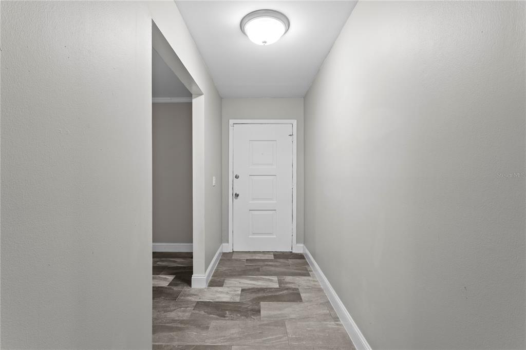 A hallway with gray walls, a white door, and gray tile flooring leads to an entrance — 6928 GREENHILL PLACE, TAMPA, FL