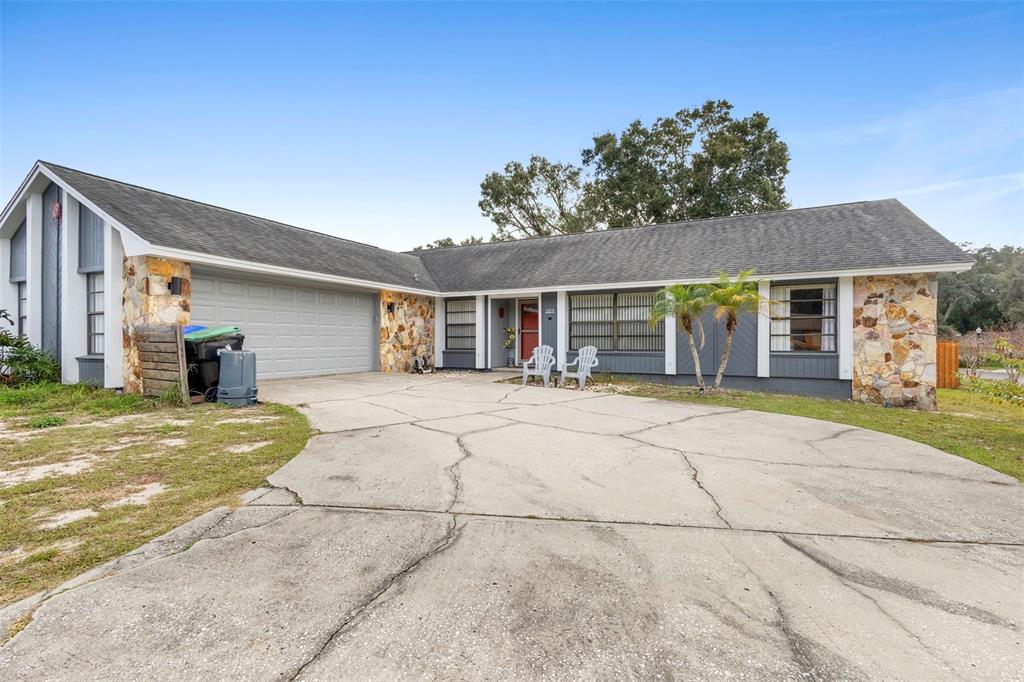 A single-story house with a stone facade, gray siding, and a cracked concrete driveway — 8611 PARK HIGHLAND DRIVE, ORLANDO, FL