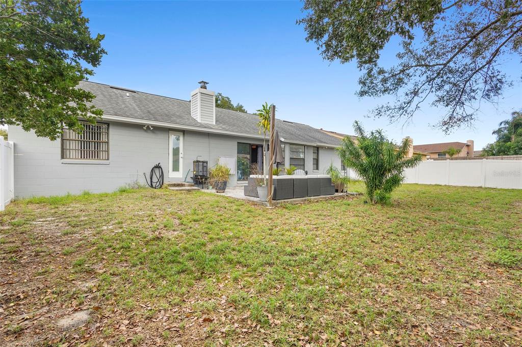 The backyard of a single-story house features a concrete patio, gray siding, and a fence — 8611 PARK HIGHLAND DRIVE, ORLANDO, FL