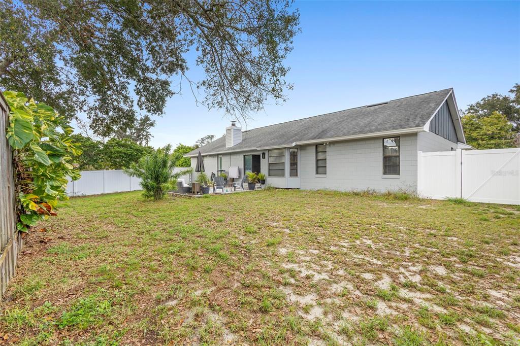 A backyard view of a gray single-story house with a patio and white vinyl fencing — 8611 PARK HIGHLAND DRIVE, ORLANDO, FL