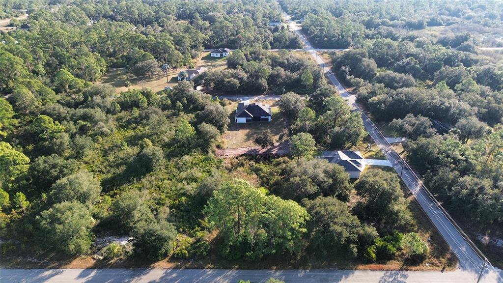 An aerial view shows several houses nestled within a wooded area near a paved road — 1502 ACACIA AVENUE, LEHIGH ACRES, FL