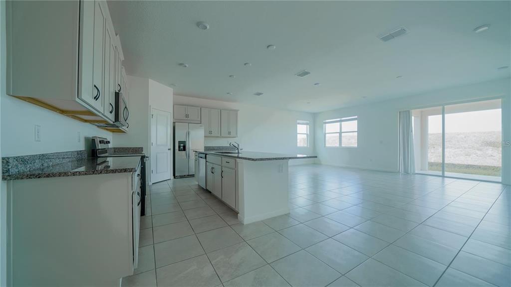 A kitchen with light-colored cabinets and granite countertops opens into a spacious tiled living area — 1194 BOARDWALK PLACE, KISSIMMEE, FL