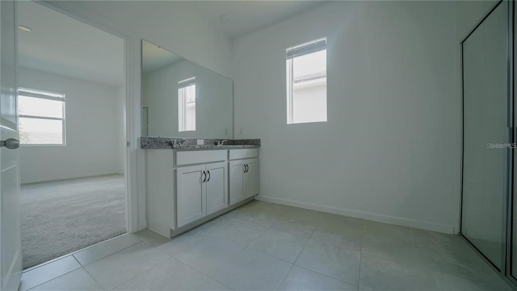 A bathroom features a double vanity with granite countertops, light cabinetry, and tiled flooring — 1194 BOARDWALK PLACE, KISSIMMEE, FL