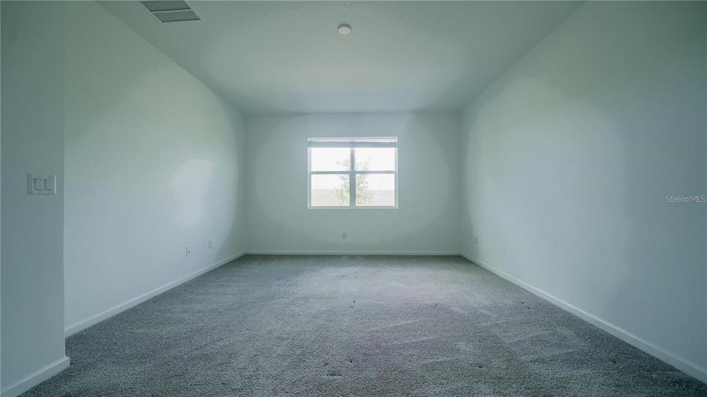 An empty room features gray carpeting, white walls, and a single window — 1194 BOARDWALK PLACE, KISSIMMEE, FL
