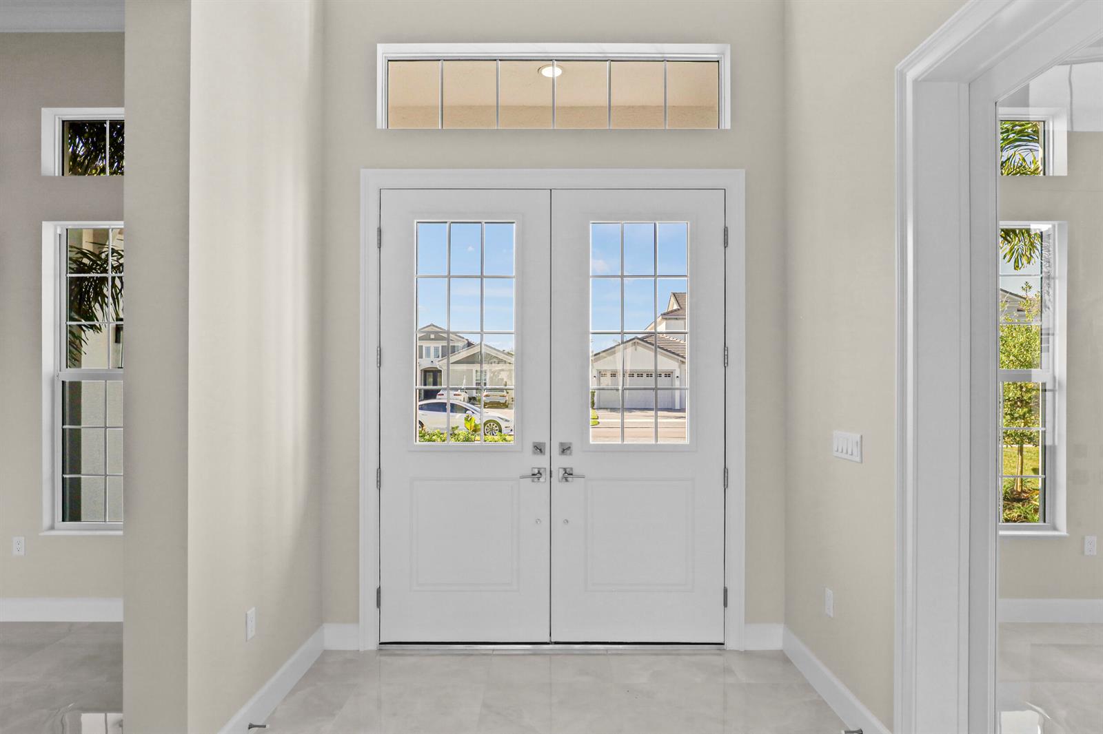 A bright entryway features double white glass-paneled doors, a transom window, and light tile flooring — 14823 Wildwood Circle, Westlake FL 33470, WESTLAKE, FL