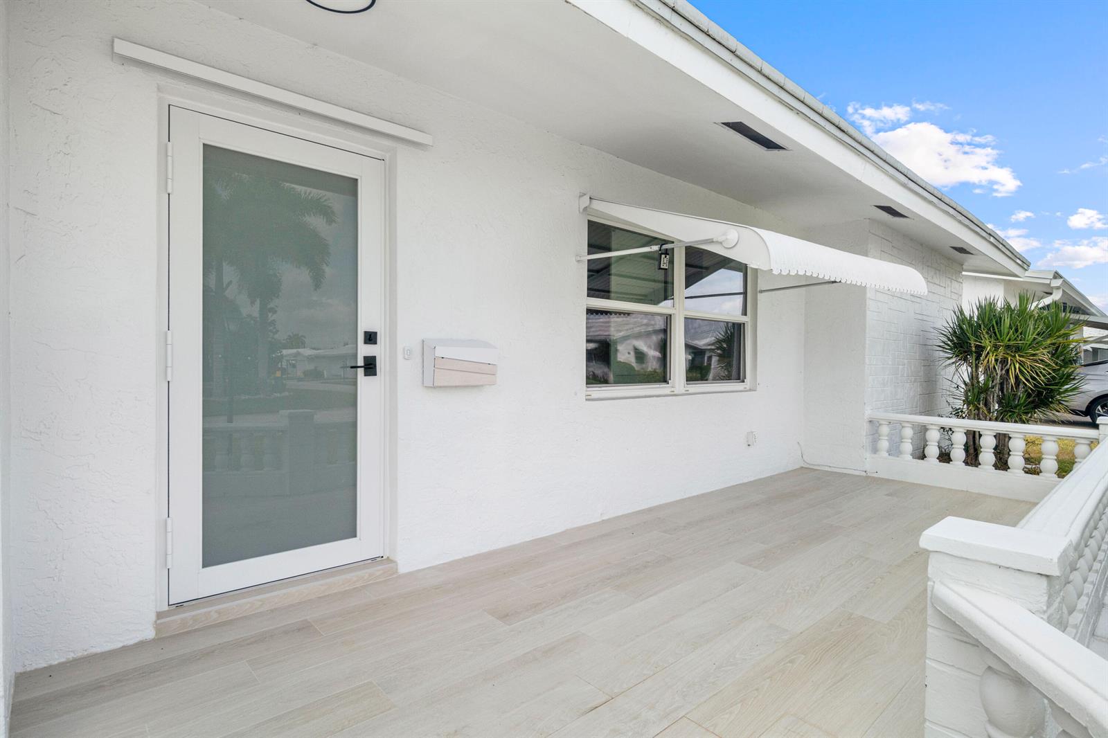 A white exterior porch features a glass-paneled door, a window with an awning, and tile flooring — 1304 SW 23rd Street, Boynton Beach FL 33426, BOYNTON BEACH, FL