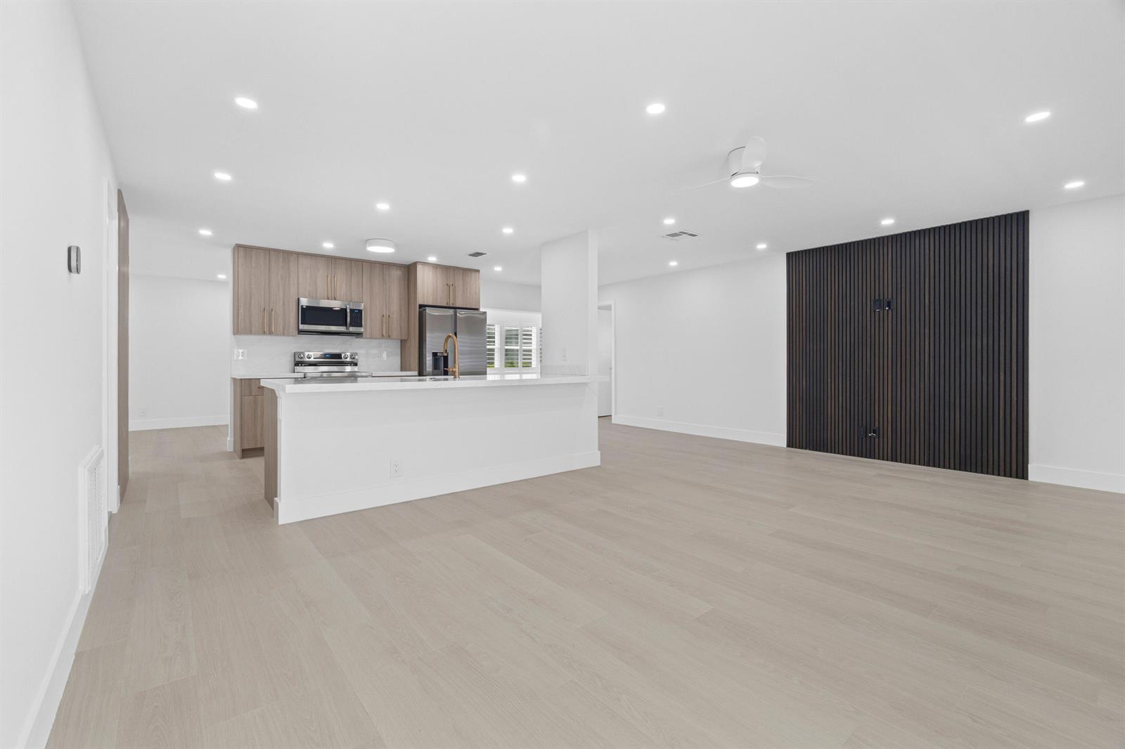 A modern open-concept kitchen features light wood cabinetry, a white island, and a slatted wall — 1304 SW 23rd Street, Boynton Beach FL 33426, BOYNTON BEACH, FL