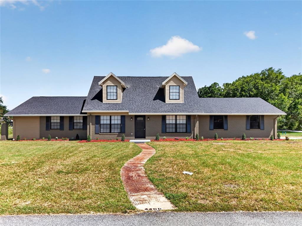 A single-story brick house with a dark shingled roof and two dormer windows — 4400 LAKE TRUDY DRIVE, ST CLOUD, FL