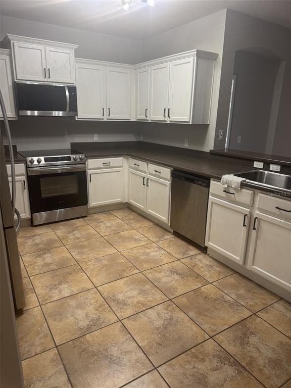 A kitchen features white cabinets, dark countertops, stainless steel appliances, and tan tile flooring — 3504 PORTVIEW COURT, KISSIMMEE, FL