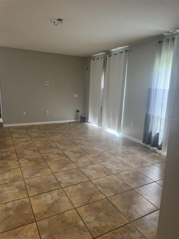 An empty living room features light gray walls, beige tile flooring, and floor-to-ceiling white curtains — 3504 PORTVIEW COURT, KISSIMMEE, FL