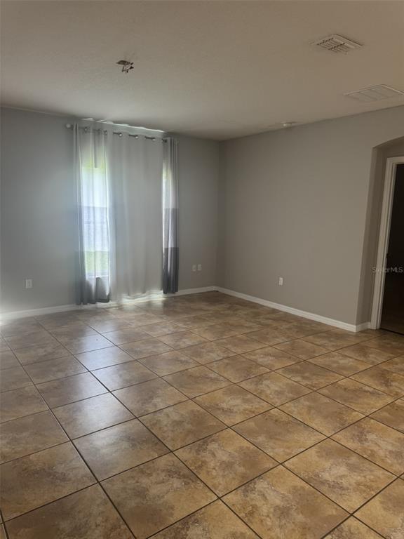 An empty room with light gray walls, tan tile flooring, and floor-to-ceiling curtains — 3504 PORTVIEW COURT, KISSIMMEE, FL