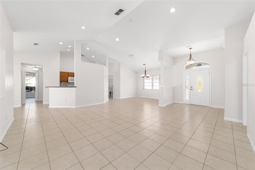 An open-concept living area features light-colored tile flooring, vaulted ceilings, and a white front door — 4560 NW 5TH COURT, OCALA, FL