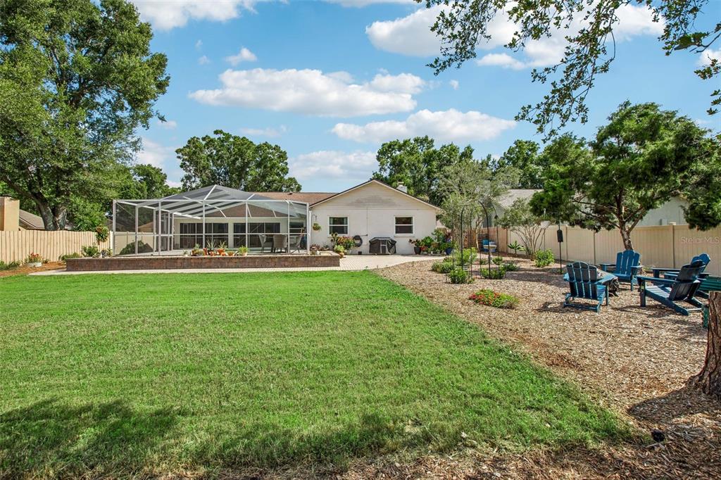 A backyard features a screened-in patio, a grassy lawn, and a gravel area with chairs — 3949 APPLETREE DRIVE, VALRICO, FL